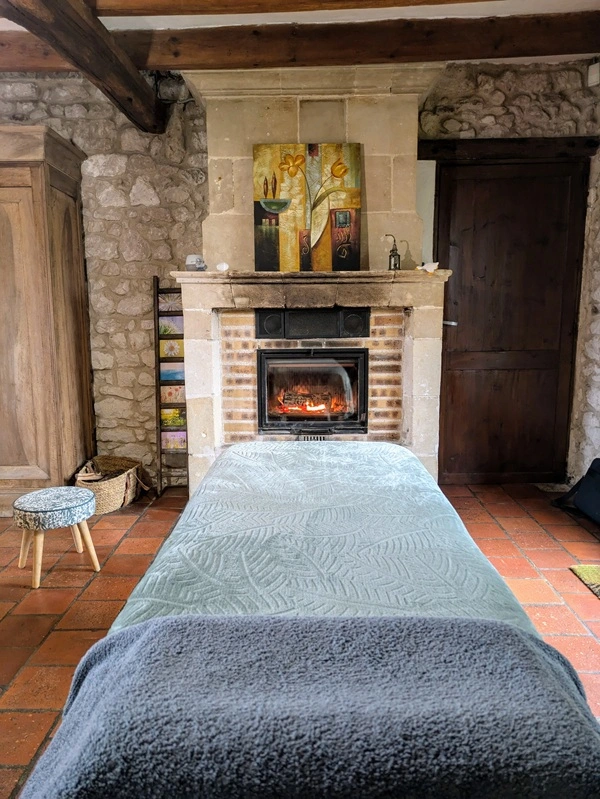 Salle de massage chaleureux avec table de soin devant une cheminée en pierre, feu allumé