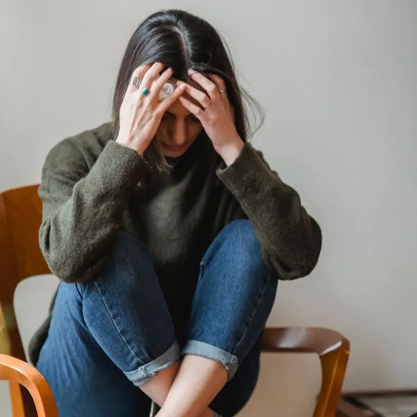 Femme anxieuse assise, lea tête entre les mains.