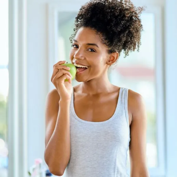 Femme souriante en pleine forme croquant une pomme, symbole de santé et bien-être